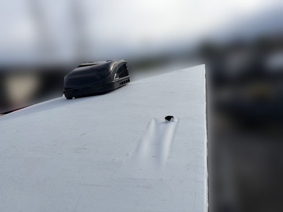 Puncture in a white RV roof membrane next to a rooftop air conditioner